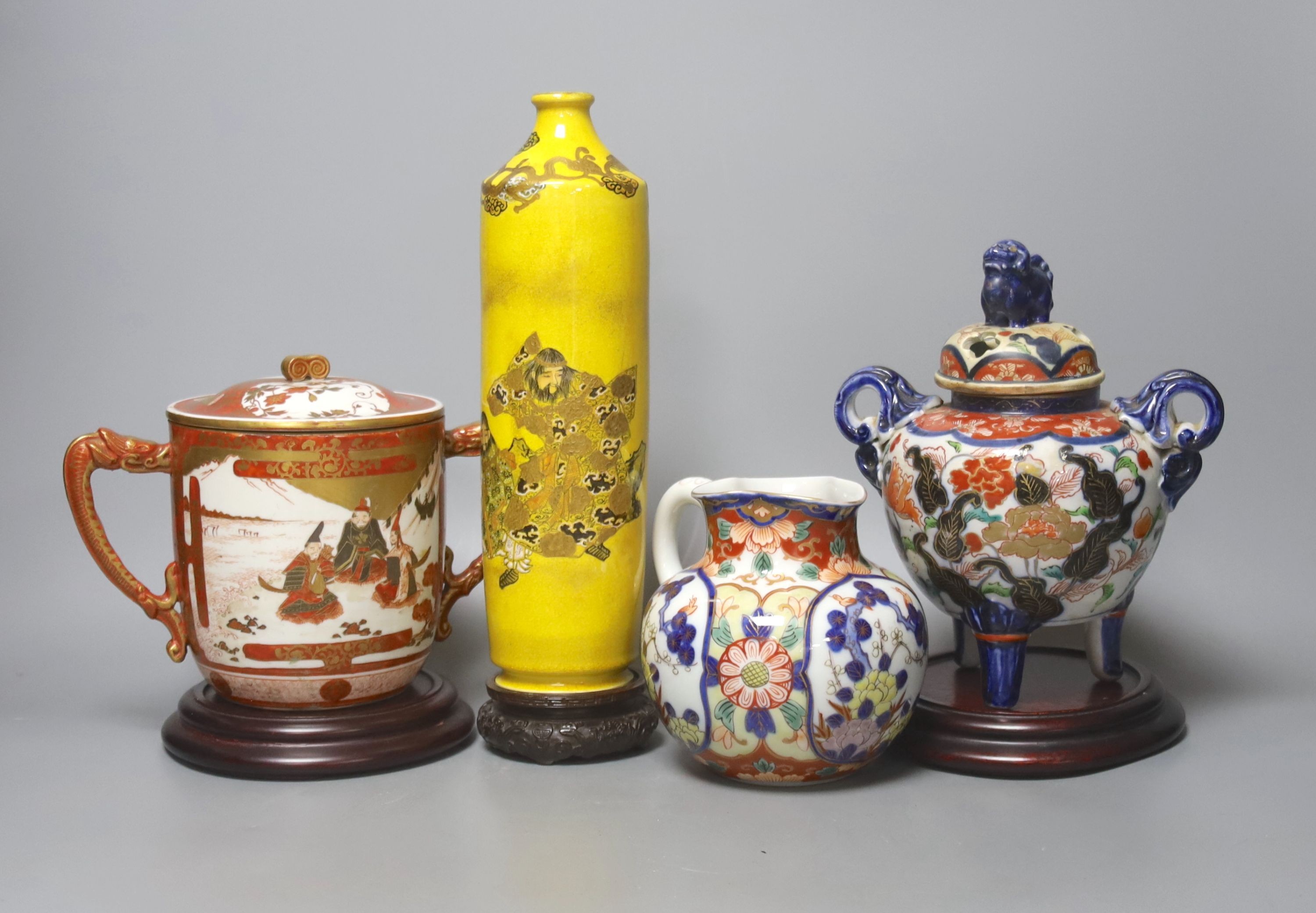 A Satsuma yellow ground vase, a Kutani twin handled cup and cover, a Fukugawa Imari jug and an Imari koro and cover 27cm, three wood stands